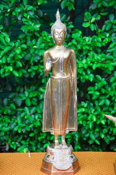 A Statue of the Monday Buddha Posture sitting on a brown table in front of some green plants
