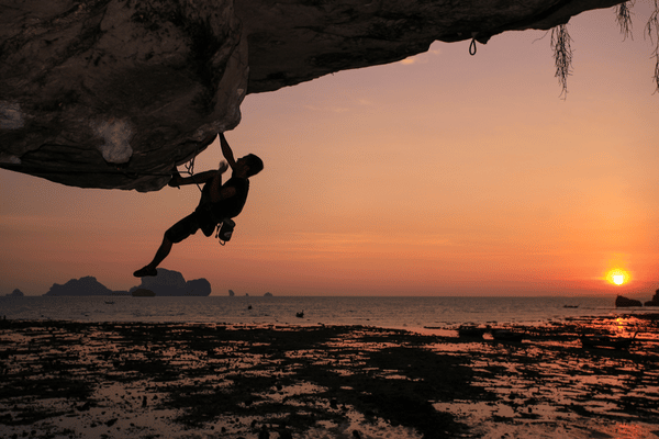 An experienced rock climber hanging off a cliff at Tonsai beach during the sunset hours