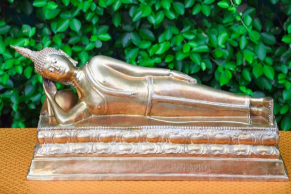A Statue of the Tuesday Buddha Posture sitting on a brown table in front of some green plants