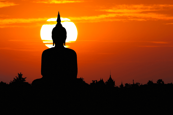 big buddha with a sun setting in the background