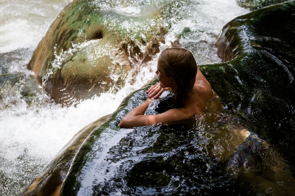 a woman bathing in the hot springs while leaning against a rock