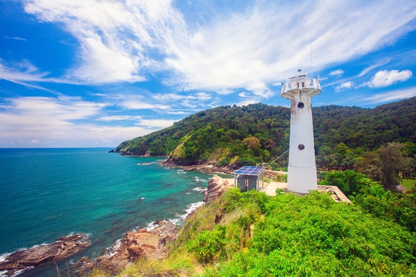 a wide screen shot showing the white lighthouse situated on the top of koh lanta overlooking the blue waters below