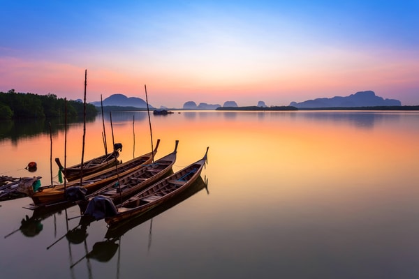 four longboats await their fisherman while anchored at sunset in the andaman sea