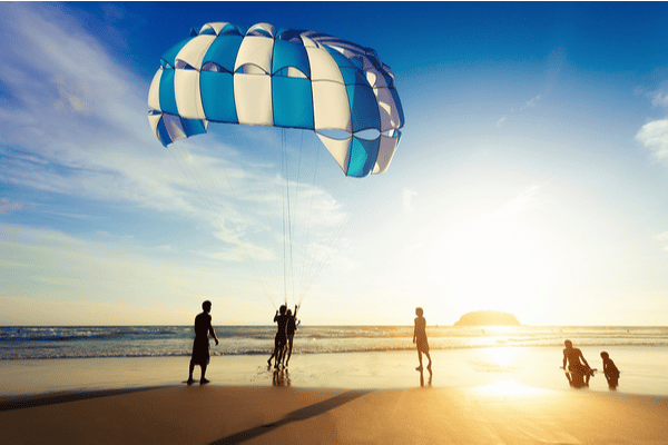 a group of 5 people launching a parasail as the sun sets in the background