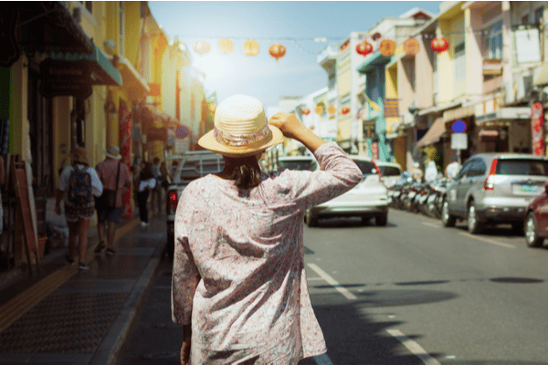 a white woman walking down Thalang Road holding onto her straw hat