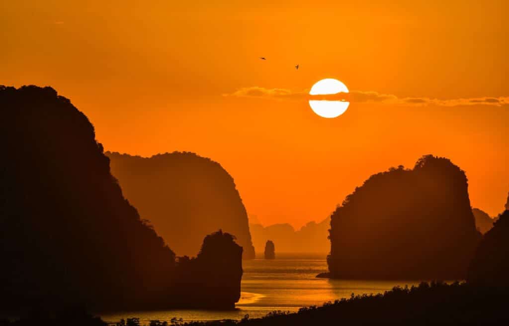the sun sets behind the limestone cliffs of phang nga bay