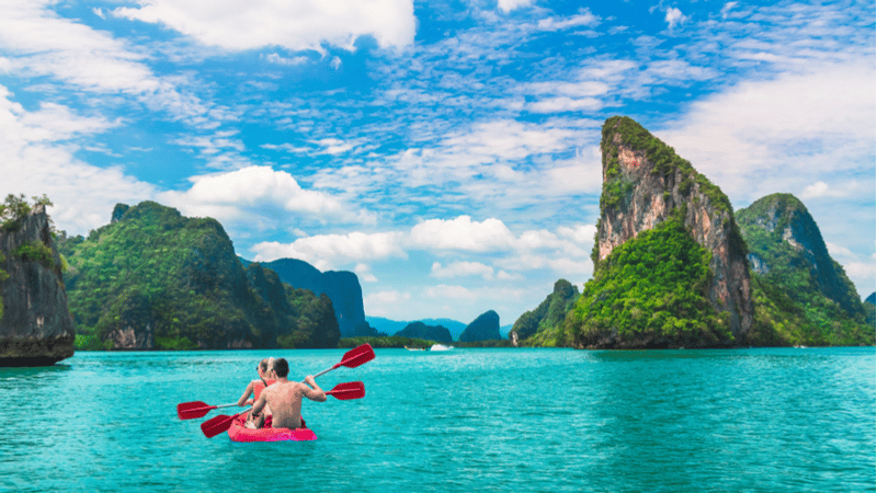 A couple kayaking in Ko Tapu, surrounded by towering limestone cliffs and clear waters.