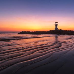 A lighthouse on the beach at sunset.