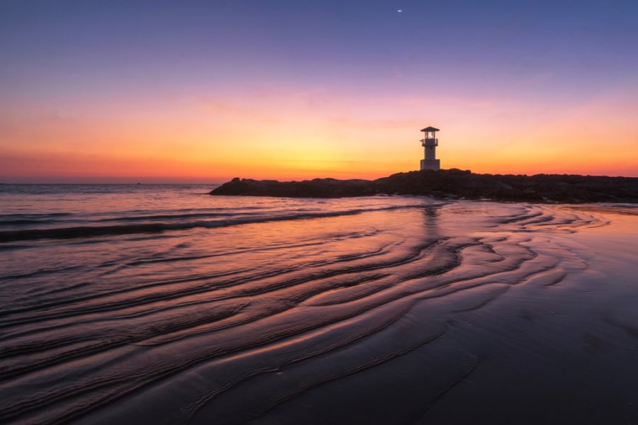 A lighthouse on the beach at sunset.