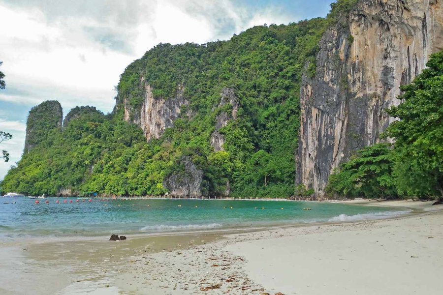 A beautiful beach with crystal clear water, white sand, and towering limestone cliffs covered in lush greenery.