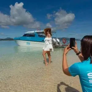 A woman capturing a photo of a boat on the beach, in front of Simba Sea Trips boat