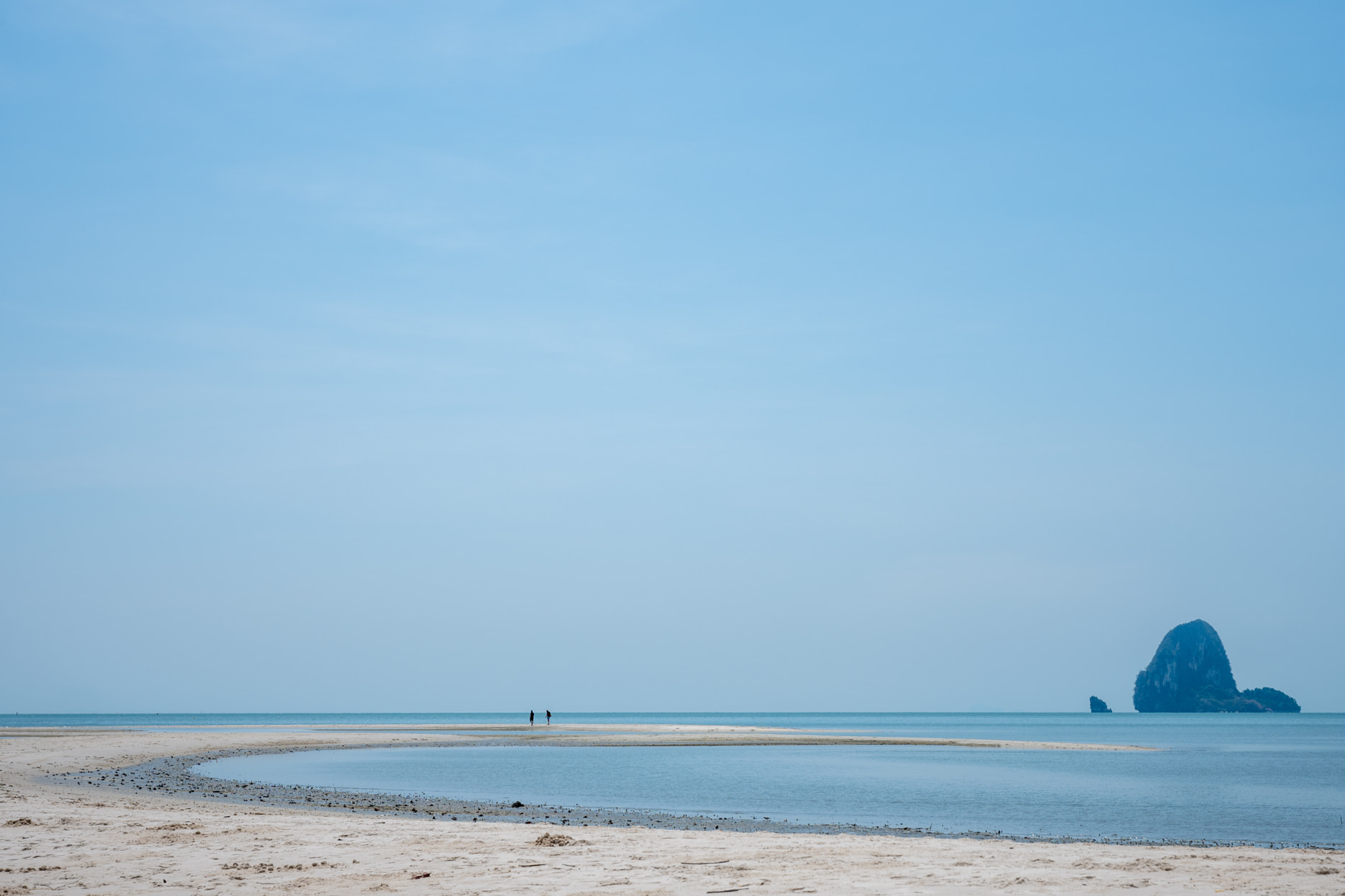 Calm sandy beach and shallow lagoon at Coconut Island Phuket with a distant limestone islet on the horizon.
