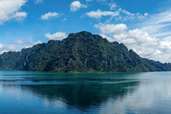 Panoramic view of Khao Sok’s limestone mountains reflected in the calm emerald water of Cheow Lan Lake.
