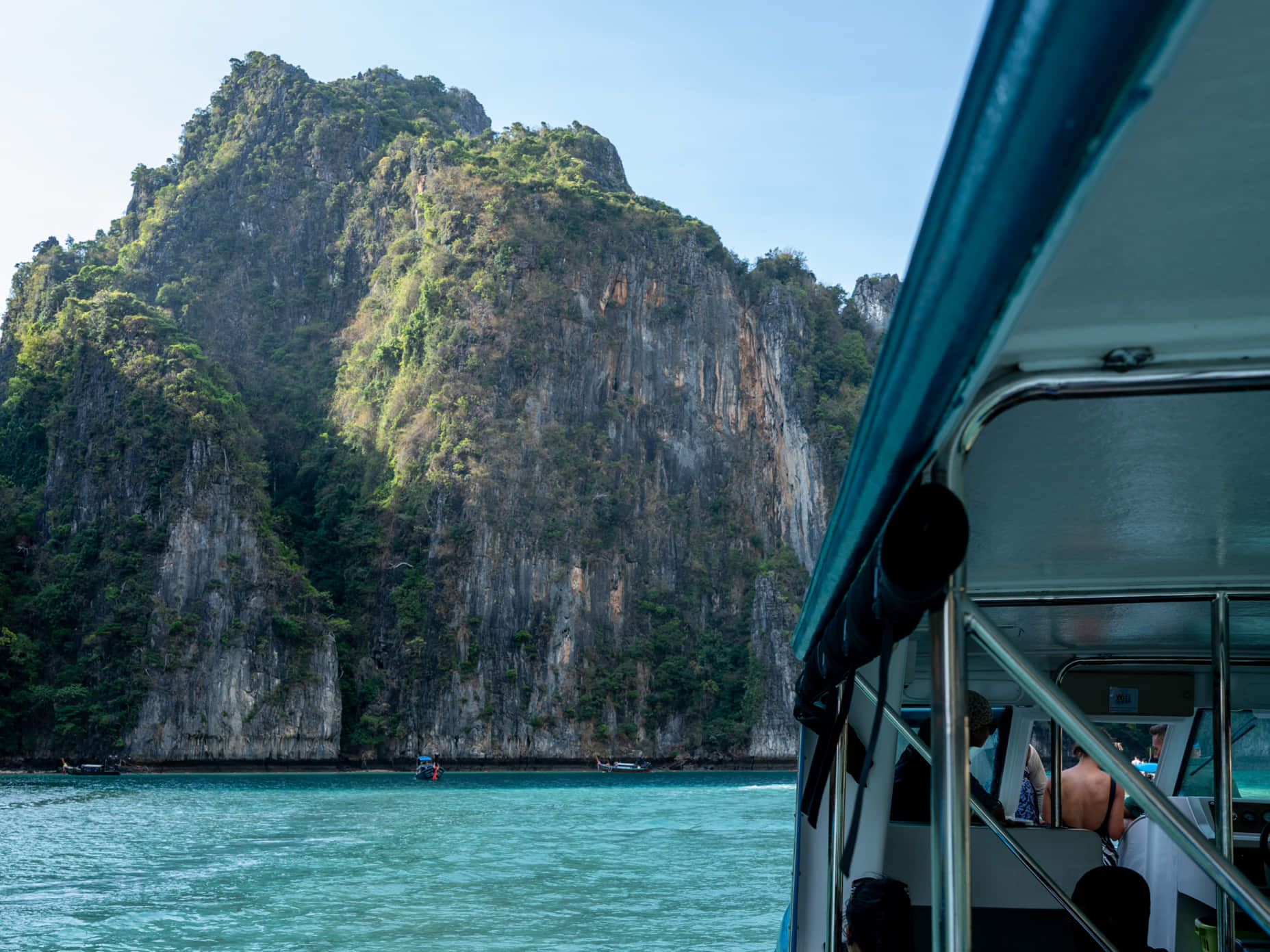 Phuket boat trips passing towering limestone cliffs and turquoise water on a sunrise cruise to the Phi Phi Islands.

