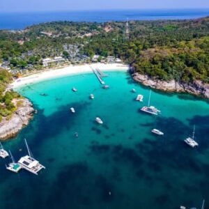 An aerial view of Koh Racha Yai with many boats anchored in the shallow waters leading to the beach.