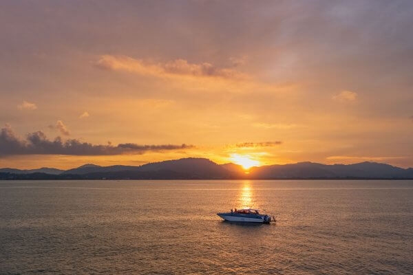 Simba Sea Trips speedboat cruising at sunset with golden light over the water and distant mountains in Phuket.